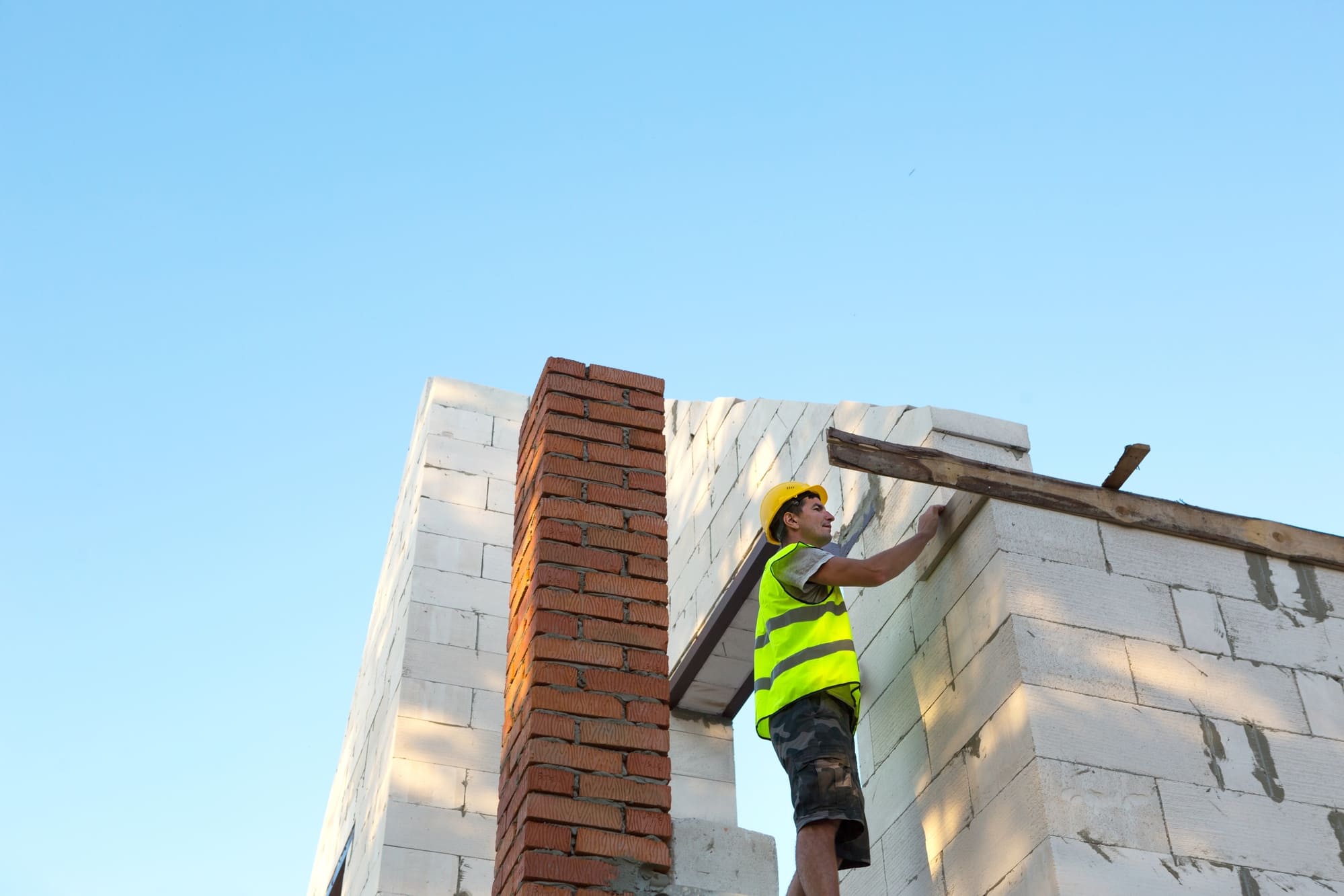 Construction worker in yellow vest and hard hat working on a building.