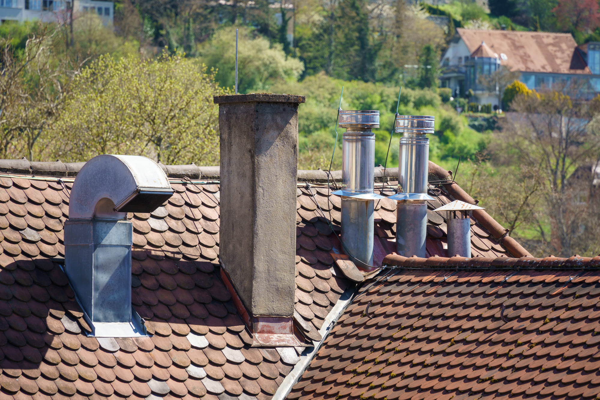 Close-up of a tiled rooftop with multiple chimneys and vents under sunlight.