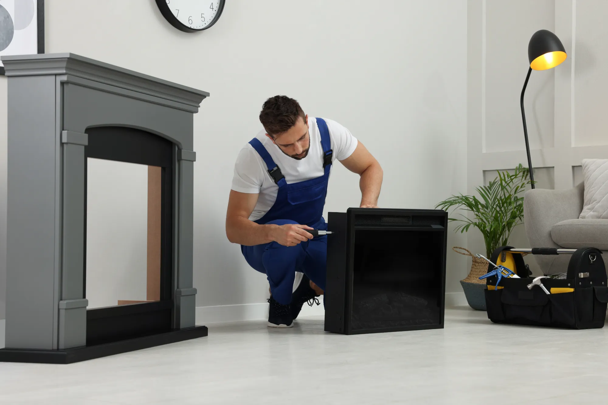 Man in blue overalls installing a black electric fireplace insert.