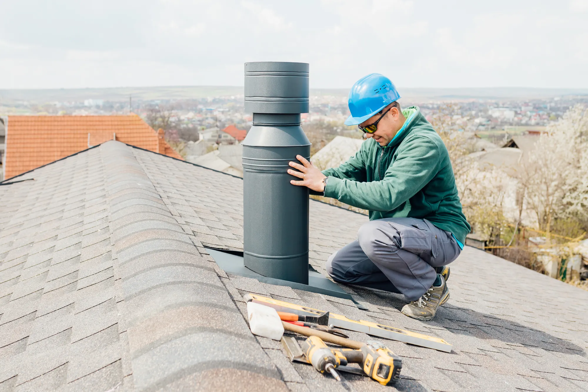 Man in blue hard hat installing a chimney pipe on a roof