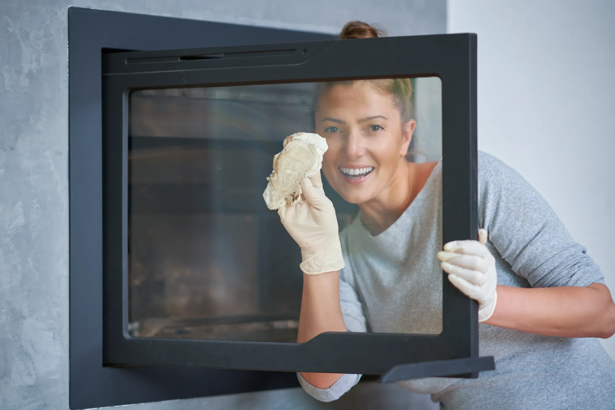 Woman in gloves cleaning a fireplace glass door with a cloth