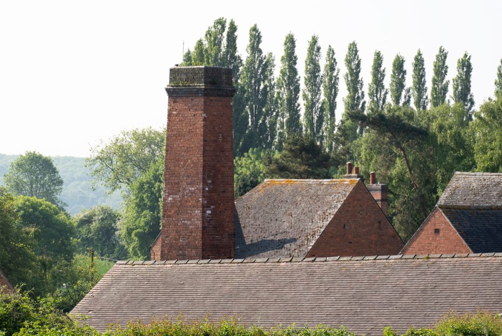 Tall brick chimney and rooftops against a bright sky and trees